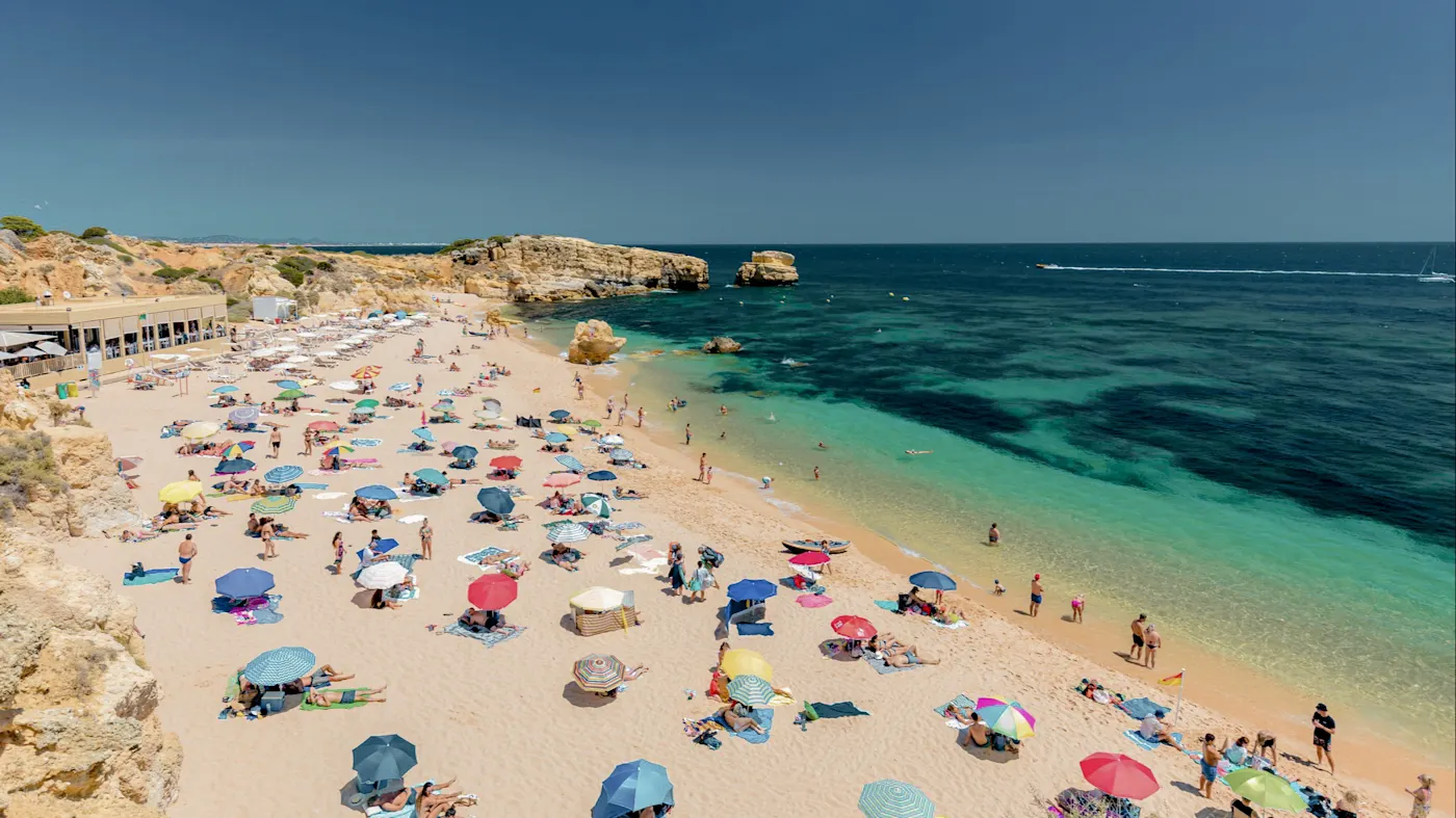 Buntes Strandleben in Albufeira, Portugal, mit Sonnenschirmen und türkisblauem Wasser.
