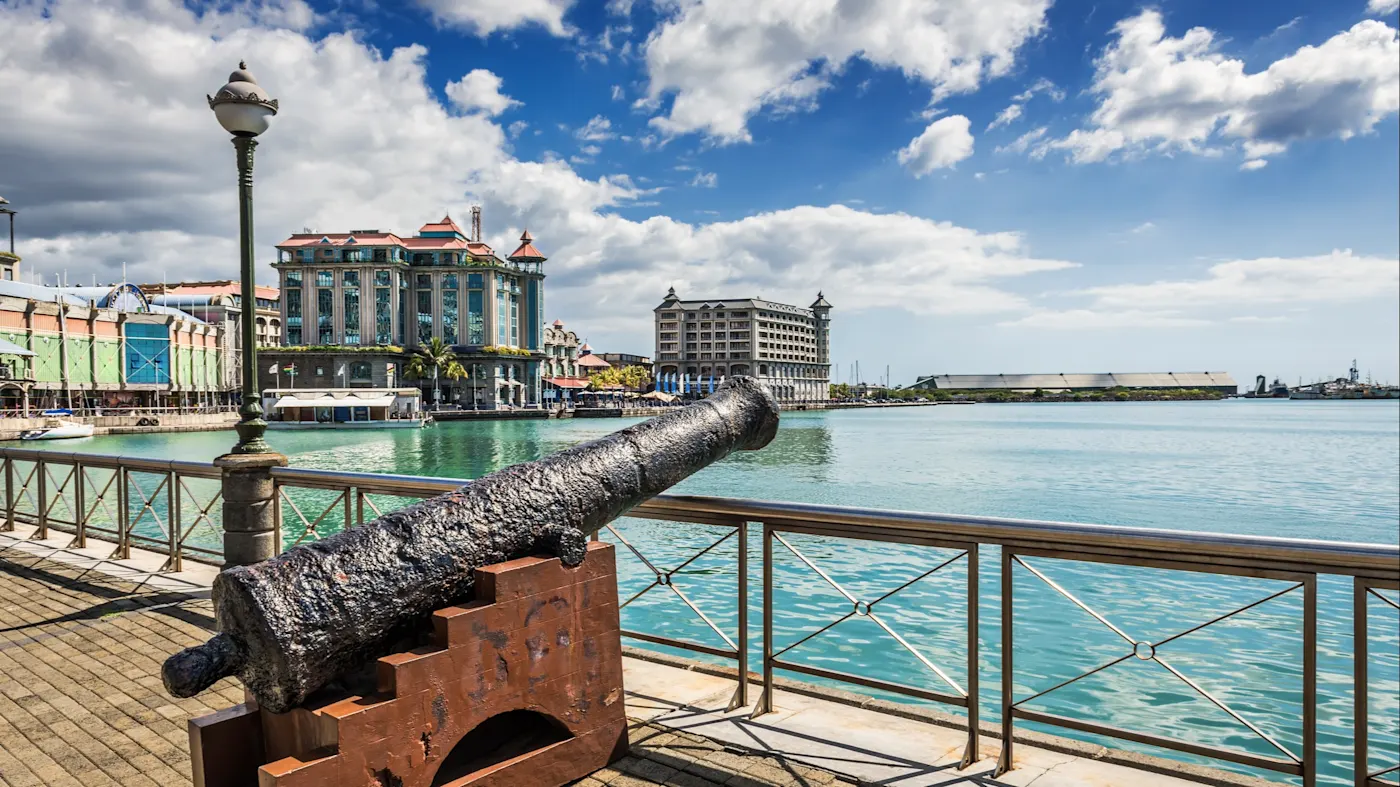 Port Louis, Mauritius. Alte Kanone am Hafen mit Blick auf moderne Gebäude am Wasser. Port Louis, Mauritius.