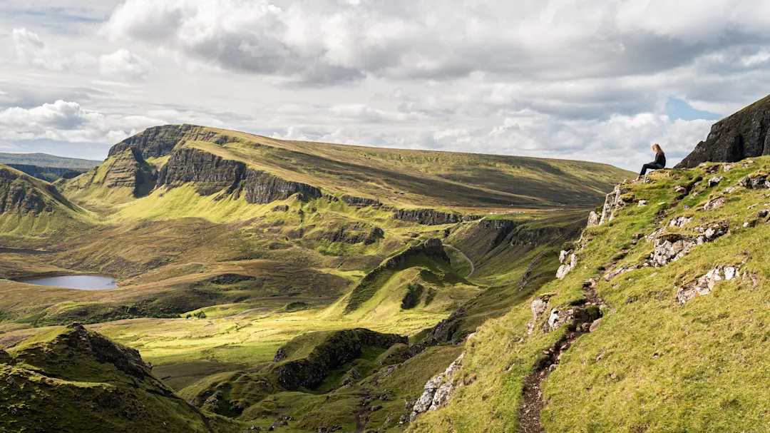 Felsige Hügel mit grünem Gras und einem Wanderer, der die Aussicht genießt. Isle of Skye, Schottland.