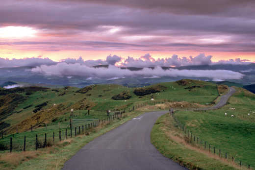 See the hilly area of Powys, pictured here with a storm cloud sunset and winding road, on a Tour of Wales