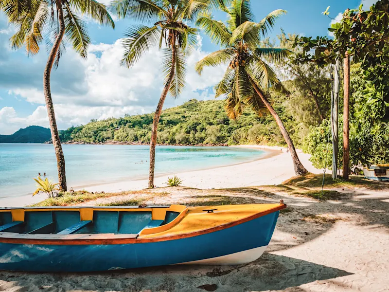 Praslin, Seychellen Blau-gelbes Boot am Sandstrand mit Palmen und türkisfarbenem Wasser. Praslin, Seychellen.