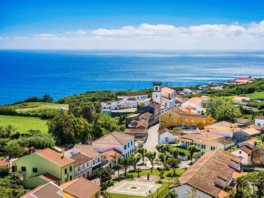 Portugal, Azoren, Nordeste Bunte Häuser und Kirche in einem Küstendorf mit Blick auf den Atlantik, Nordeste, Azoren, Portugal.