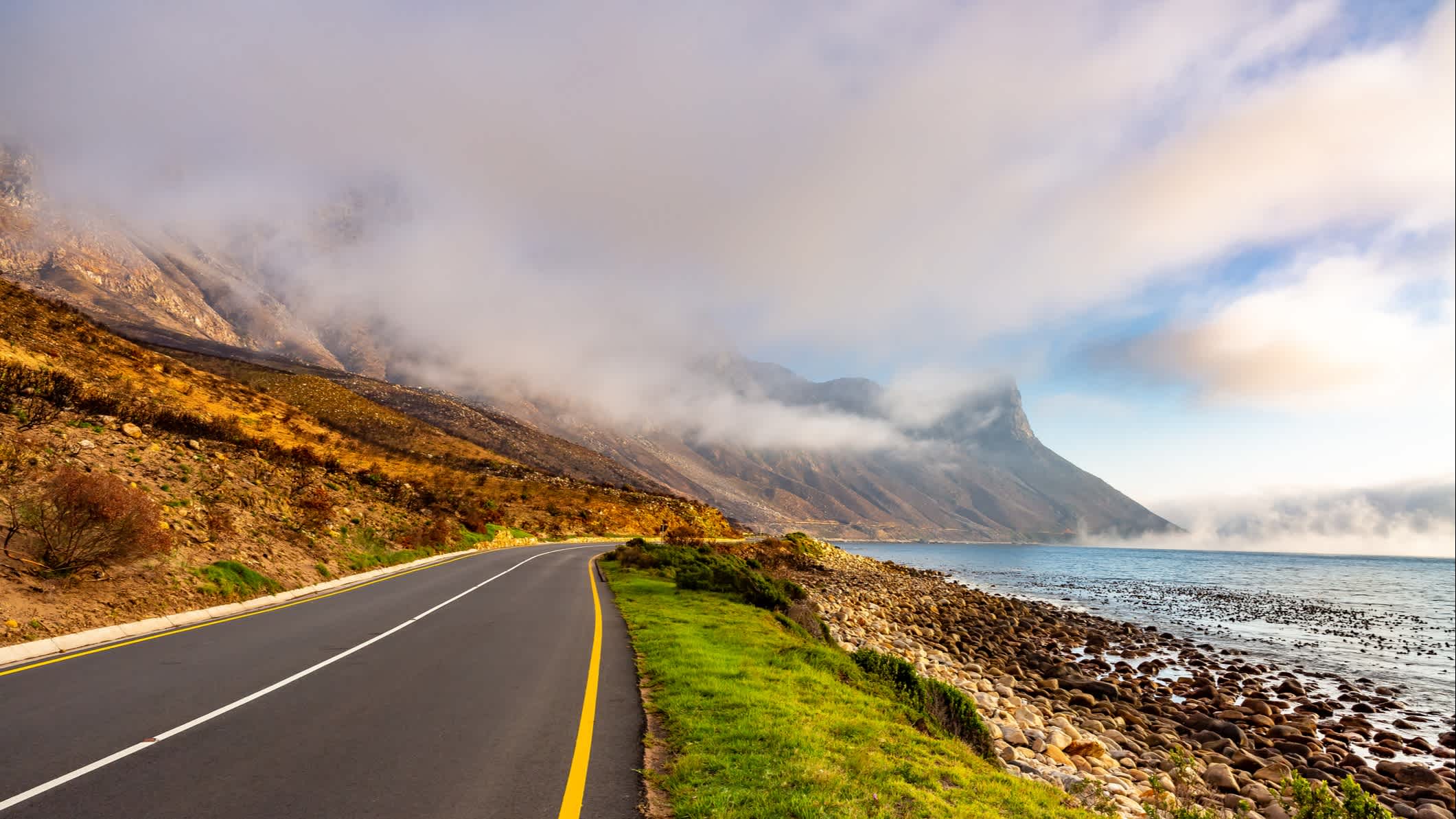 Blick auf einen Abschnitt der Garden Route mit aufsteigendem Nebel im Hintergrund und Ufer rechts