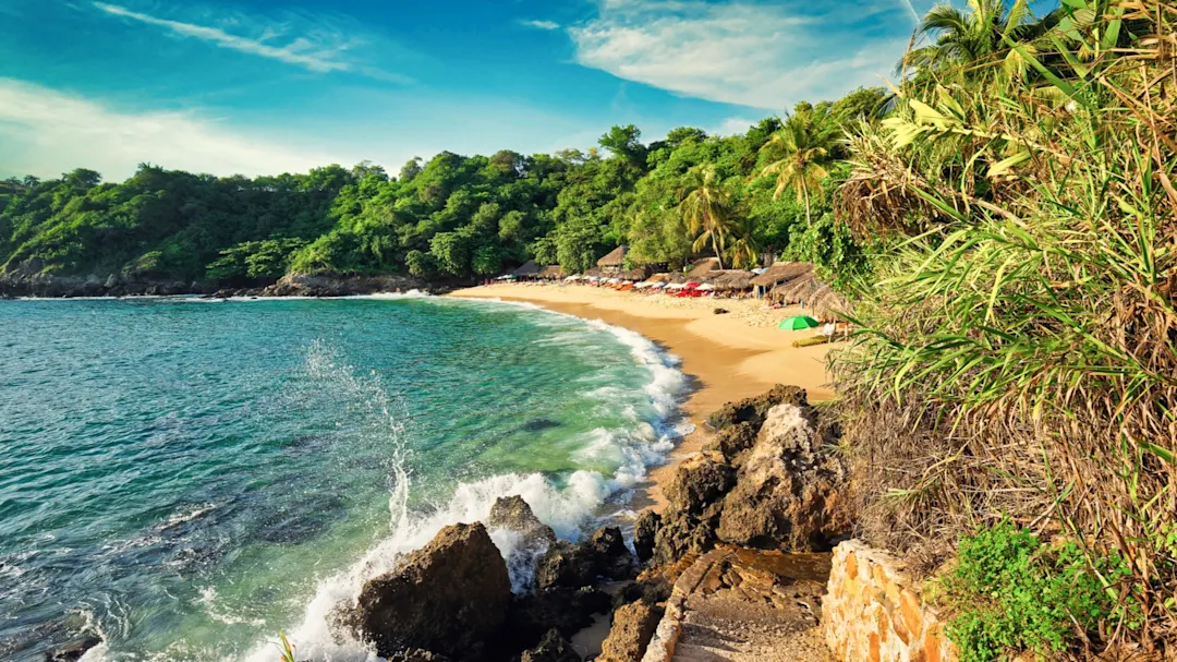 Kleine Bucht mit türkisfarbenem Wasser, goldgelbem Sand und umgeben von grüner Vegetation. Puerto Escondido, Oaxaca, Mexiko.