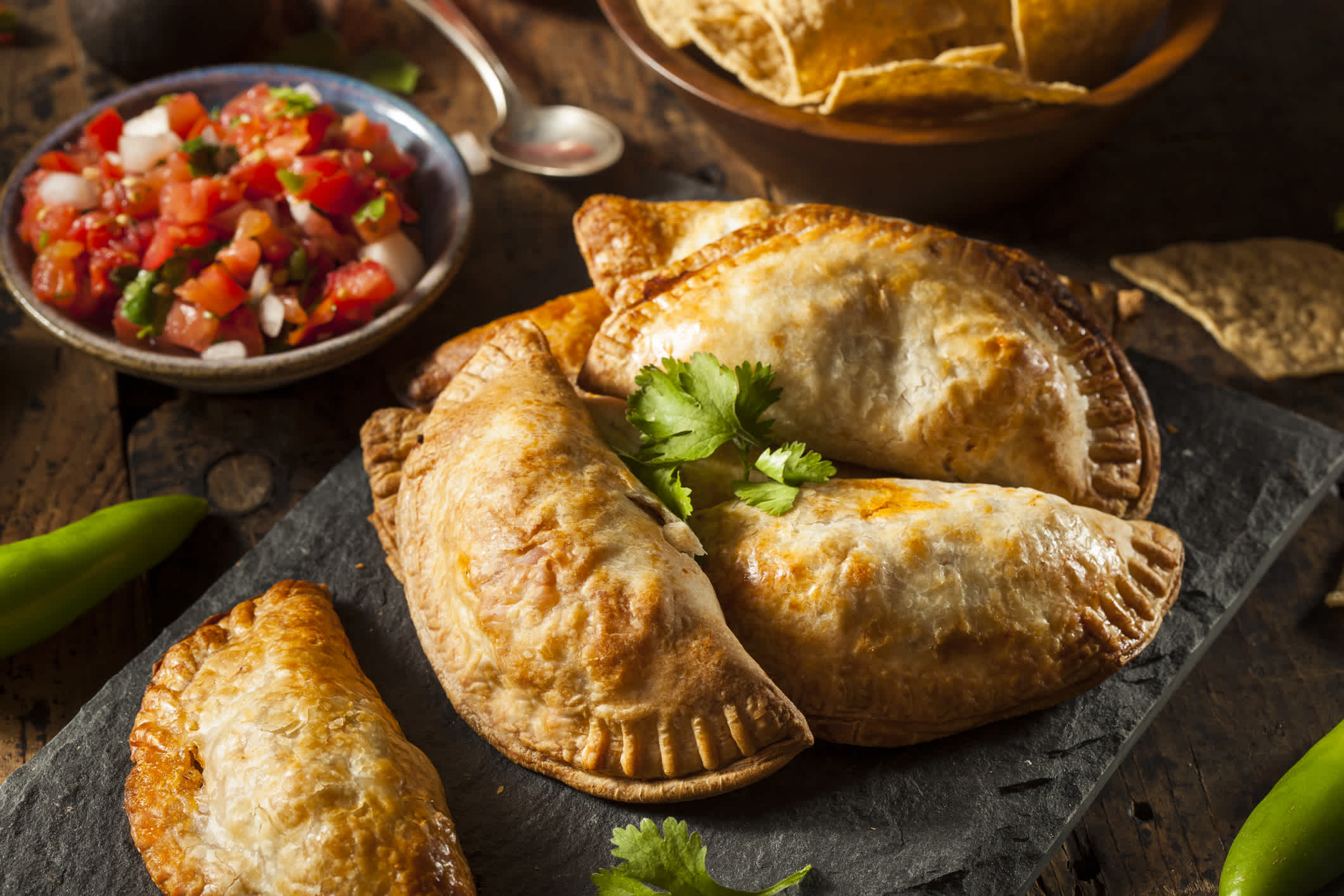 A table with empanadas and tortilla chips in the background. 