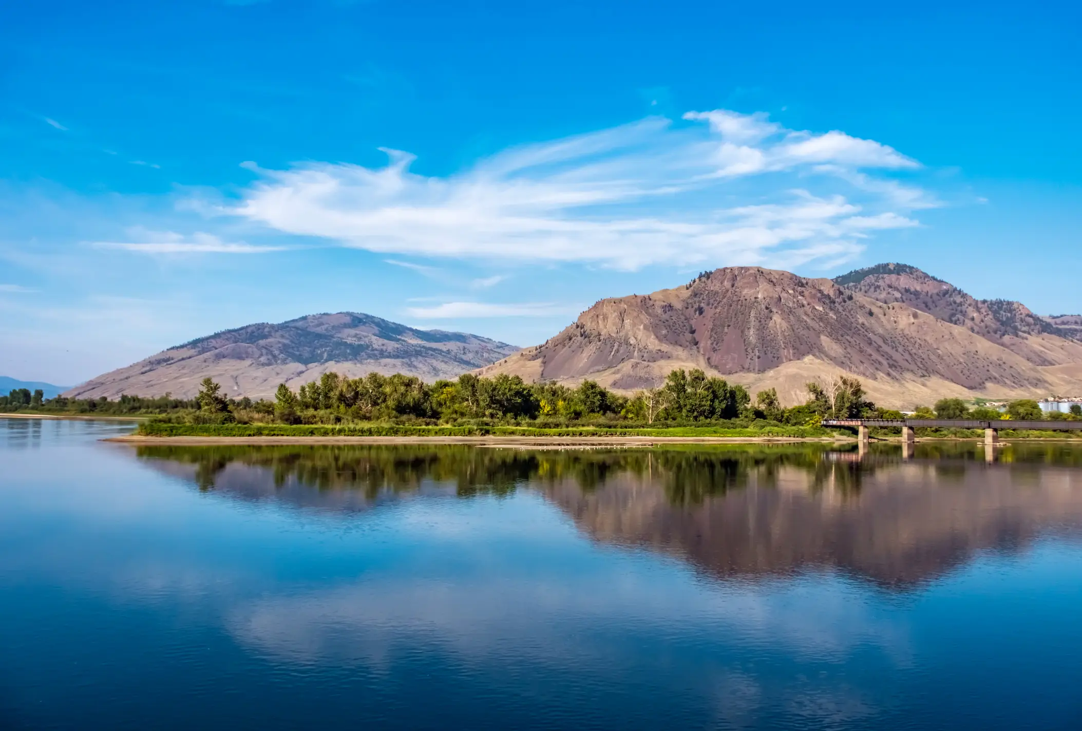 Thomson River bei Kamloops mit Bergkette und Eisenbahnbrücke in der Ferne, British Columbia, Kanada.
