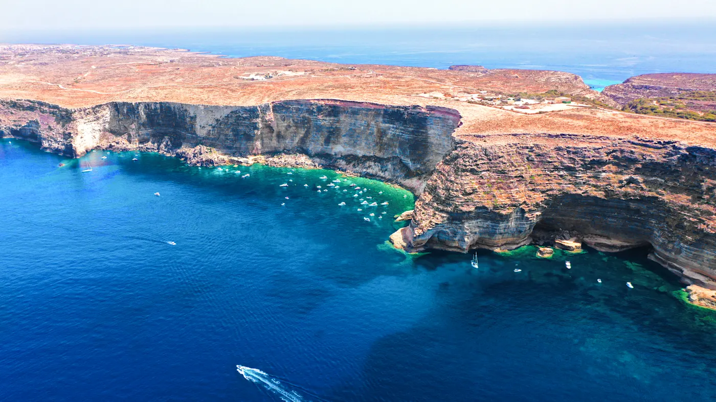 Italien, Sizilien, Lampedusa Atemberaubende Steilküste mit türkisblauem Wasser und Booten. Lampedusa, Sizilien, Italien.