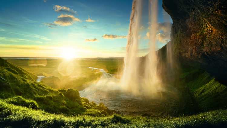 Plan a European Tour package and you'll discover incredible waterfalls, like Seljalandsfoss Waterfall in Iceland, pictured in the morning mist with the sun rising over green hills.