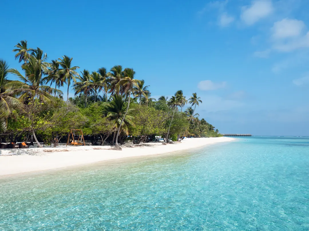 Strand auf den Malediven auf Meeru Island mit Palmen, bewölktem Himmel und Indischem Ozean.

