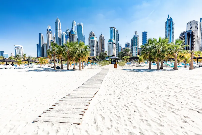 Holzweg durch weißen Sandstrand mit Palmen, Skyline im Hintergrund, Dubai, VAE