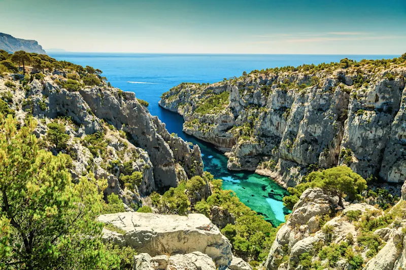 Dramatische Küstenlandschaft mit türkisblauem Wasser zwischen steilen Kalksteinfelsen und grüner Vegetation am Mittelmeer.