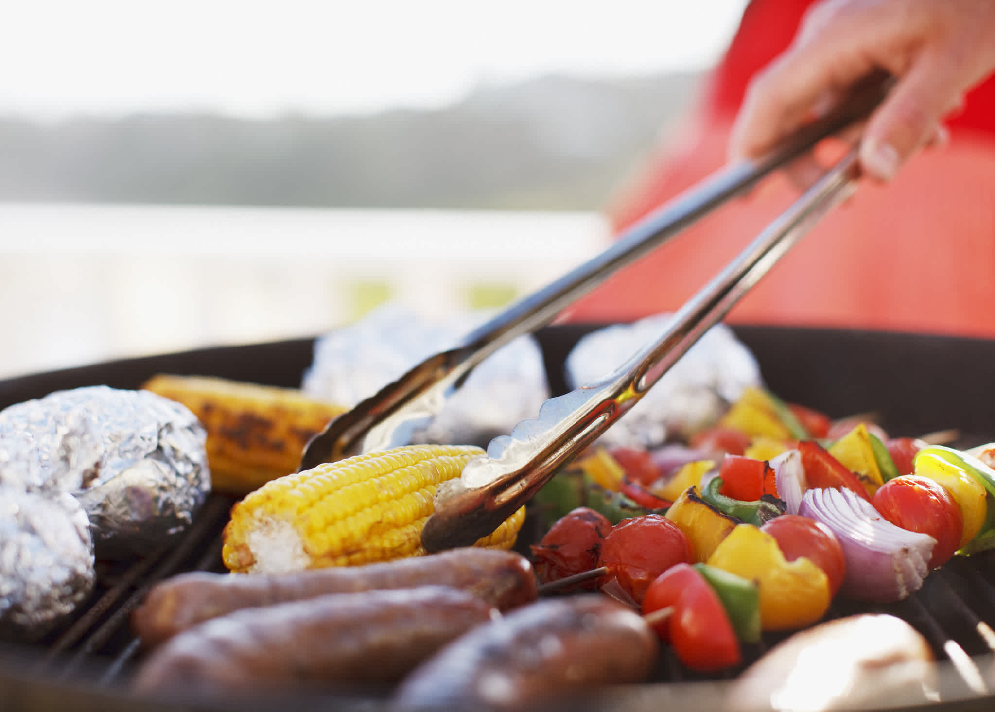Close-up of the man grilling sausages and vegetables on the barbecue. 
