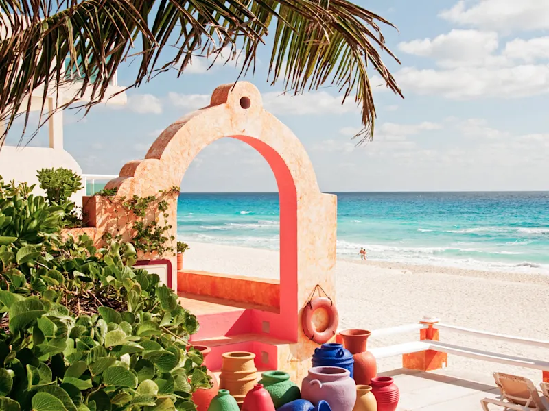 Cancún, Quintana Roo, Mexiko Blick durch ein buntes Tor auf einen tropischen Strand mit türkisfarbenem Meer. Cancún, Quintana Roo, Mexiko.