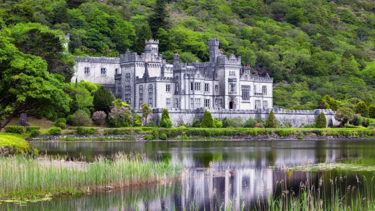 Europe, Ireland, Connemara, Kylemore Abbey surrounded by lush forest and reflected in a grass-lined pond.