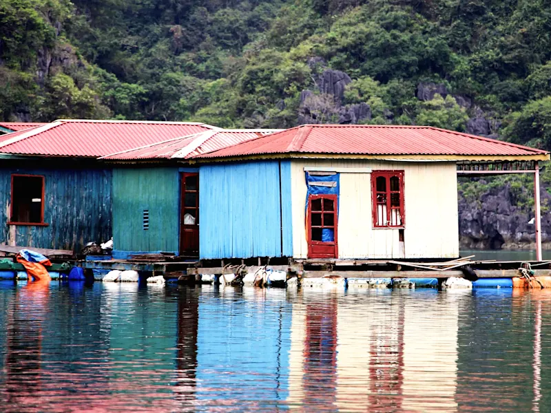 Halong, Quang Ninh, Vietnam. Buntes schwimmendes Haus auf der Halong-Bucht, umgeben von grünen Felsen. Halong, Quang Ninh, Vietnam.