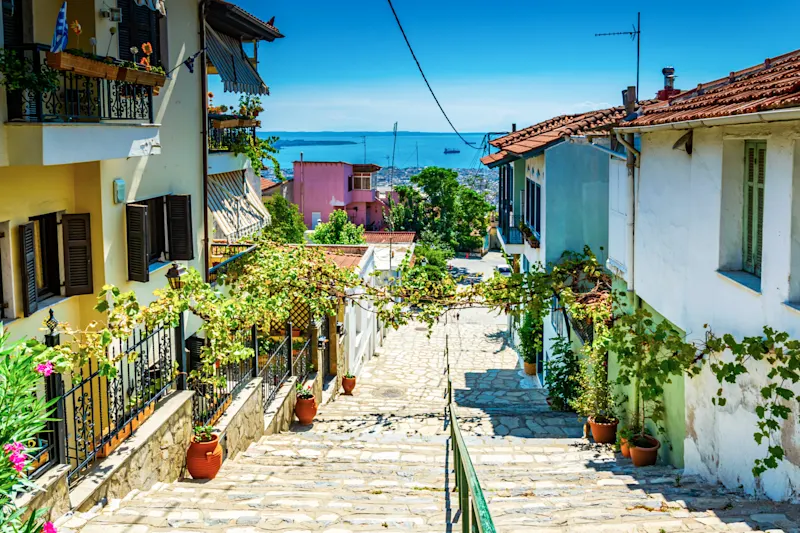 Thessaloniki, Makedonien, Griechenland. Blick auf eine enge Gasse in der Altstadt von Thessaloniki mit dem Ozean im Hintergrund