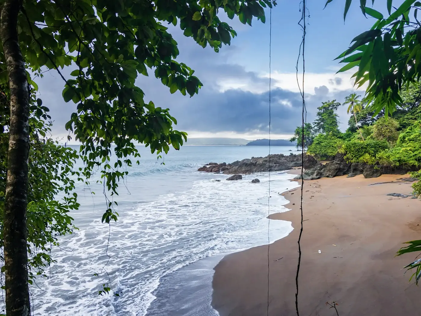 Costa Rica, Puntarenas, Drake Bay Versteckter Strand mit üppigem Grün im Vordergrund. Drake Bay, Puntarenas, Costa Rica.