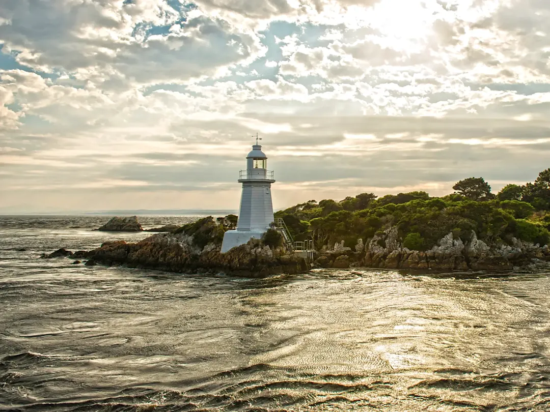 Weißer Leuchtturm auf Felsen am Meer bei Sonnenuntergang. Strahan, Tasmania, Australien.
