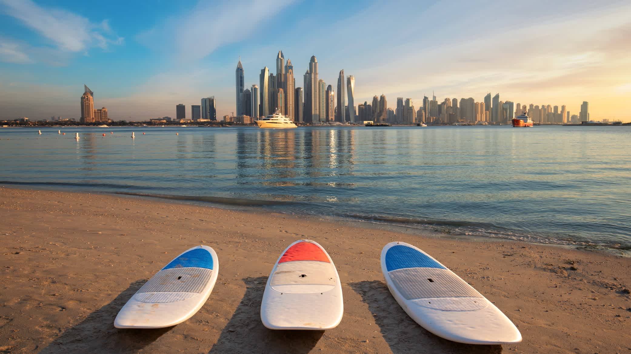 Surfbrettern am Strand mit dem Wolkenkratzer im Hintergrund, Dubai, VAE. 

