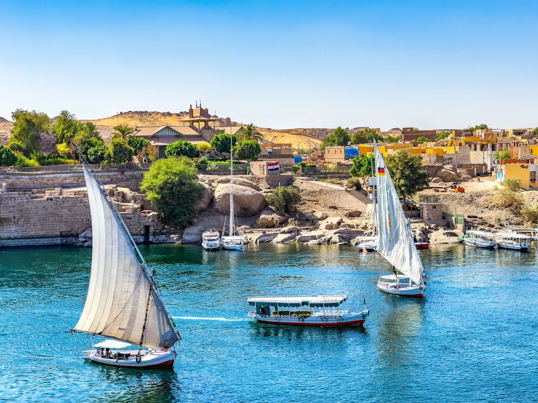 Assuan, Ägypten Blick auf den Nil mit Feluken und Motorbooten vor der Stadt und einer felsigen Insel unter blauem Himmel, in Assuan, Ägypten.