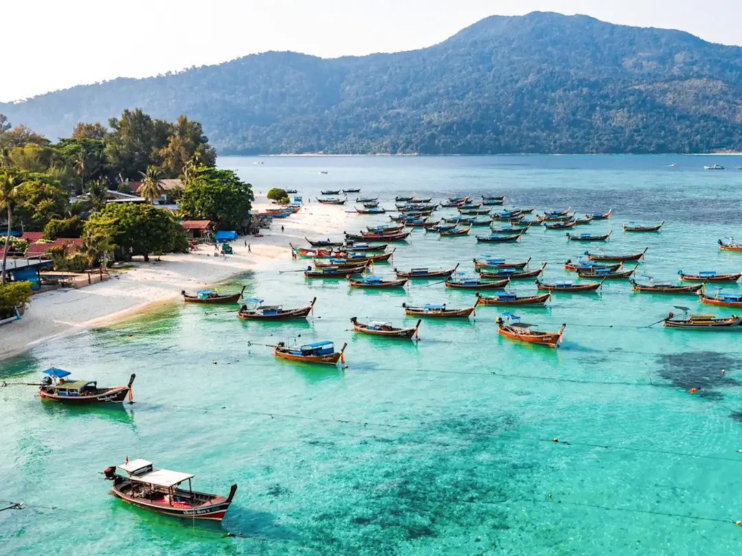 Holzboote auf kristallklarem Wasser vor tropischer Insel. Pattaya Beach, Koh Lipe, Thailand.
