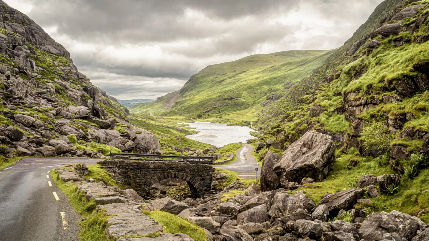 Blick auf die Berge und die Straße mit einer Brücke im Ring of Kerry, Irland.
