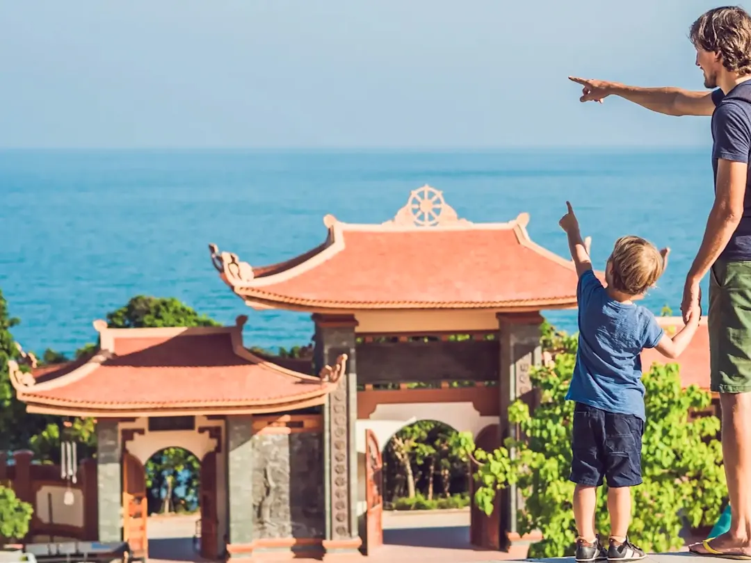 Vater und Kind zeigen auf das Meer von einem roten Tempel aus in Phu Quoc, Vietnam.