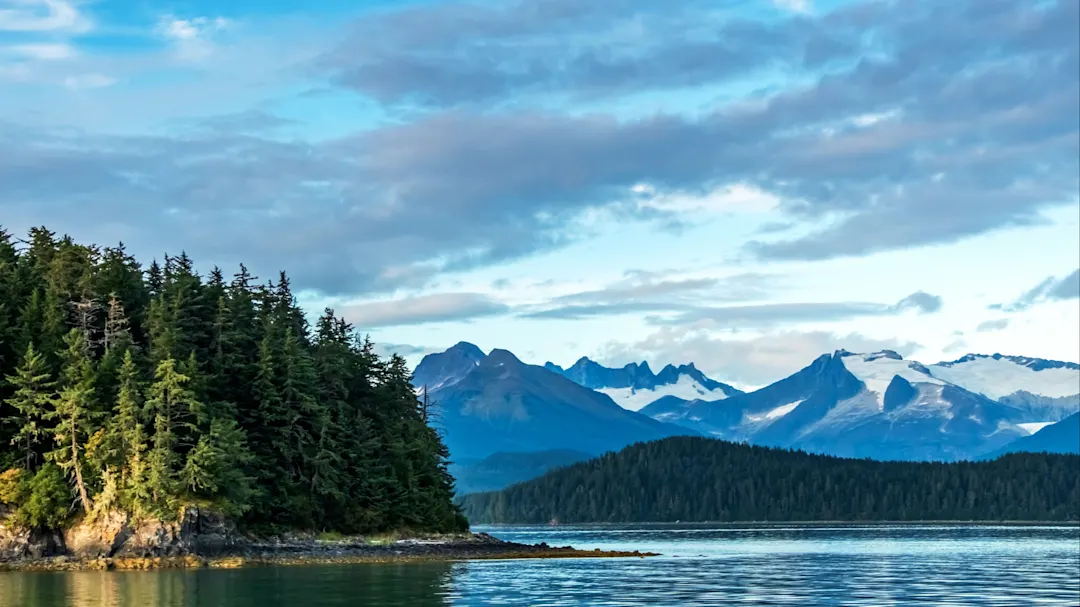 Atemberaubender Blick auf bewaldete Küste, ruhiges Wasser und schneebedeckte Berge. Juneau, Alaska, USA.