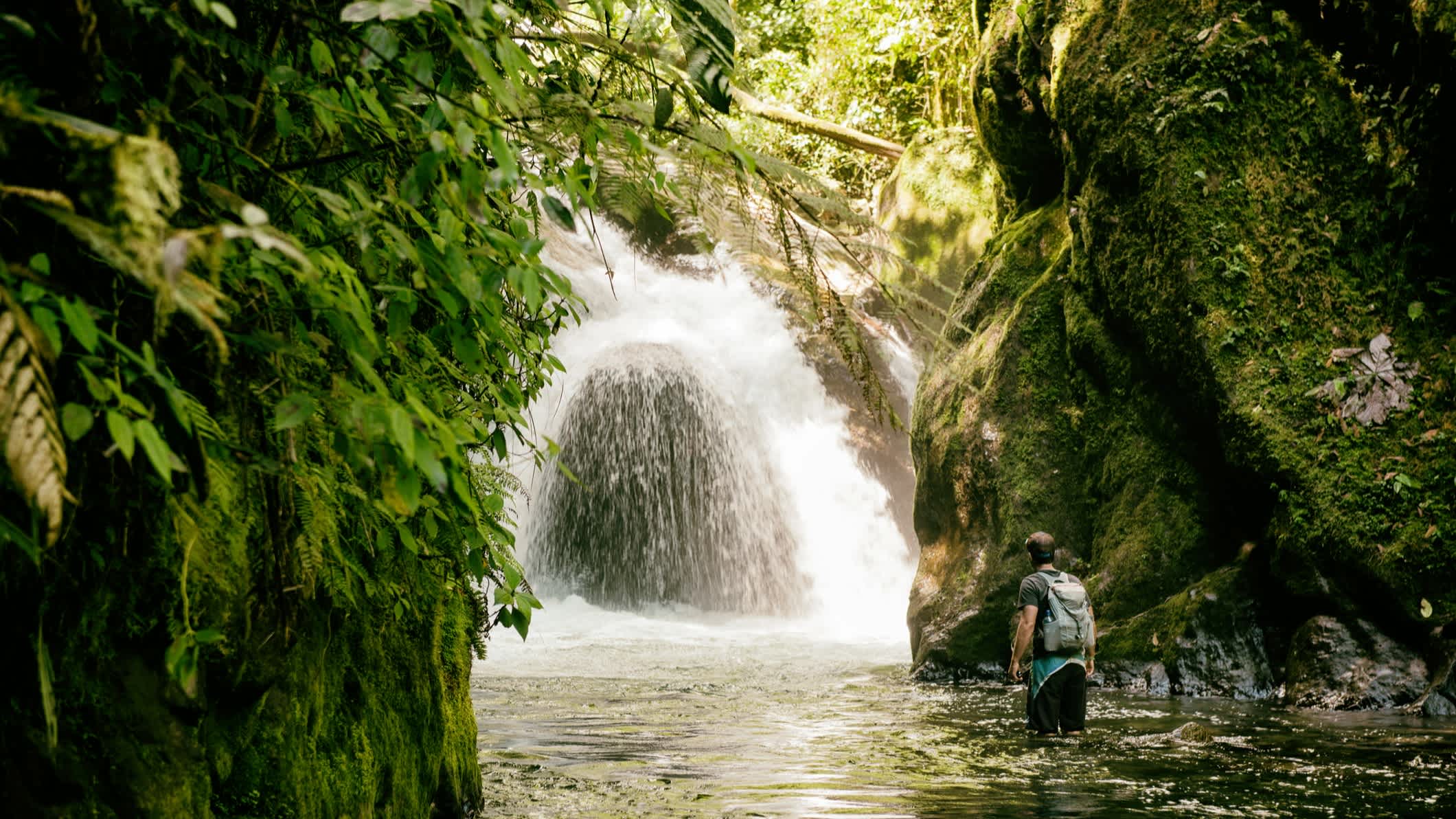 Personne avec un sac à dos marchant dans l'eau vers une cascade dans la jungle, en Équateur. 