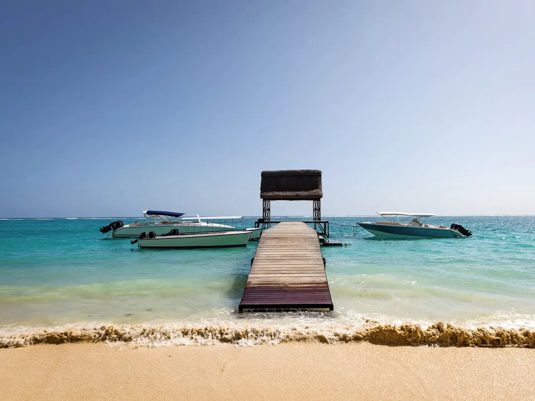 Mauritius, Strand Steg mit Booten im türkisfarbenen Wasser an einem Sandstrand, Mauritius.