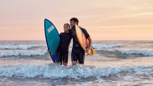 Glückliches Surferpaar, das das Meer bei Sonnenuntergang verlässt.


