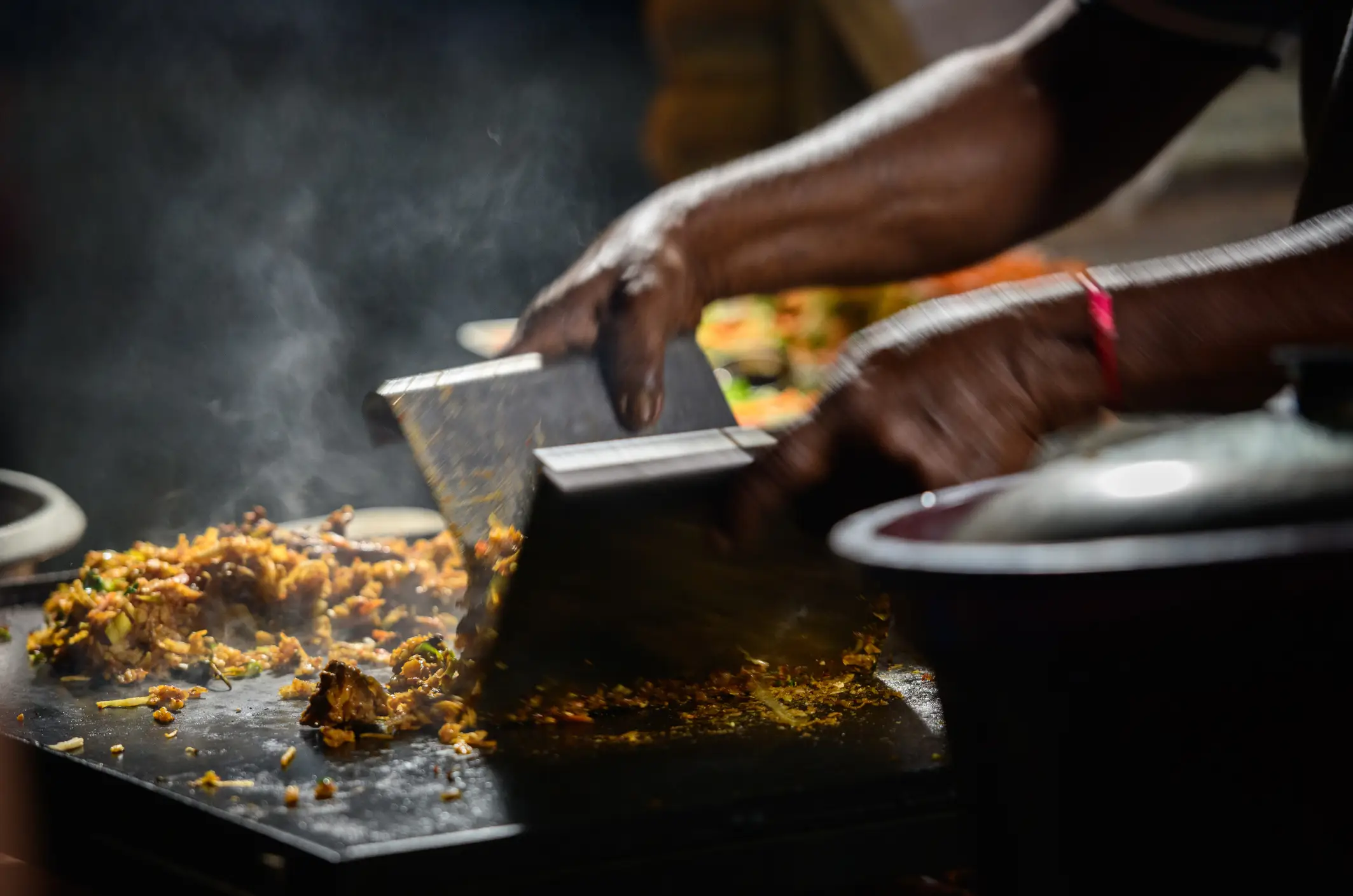 Hände des Kottu-Roti-Verkäufers, der Kottu auf einer heißen Stahlgrillplatte zubereitet