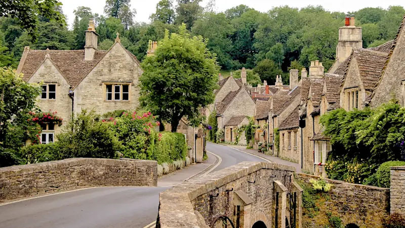 Malerische Straße mit traditionellen Steinhäusern in grüner Landschaft, Castle Combe, Cotswolds, England