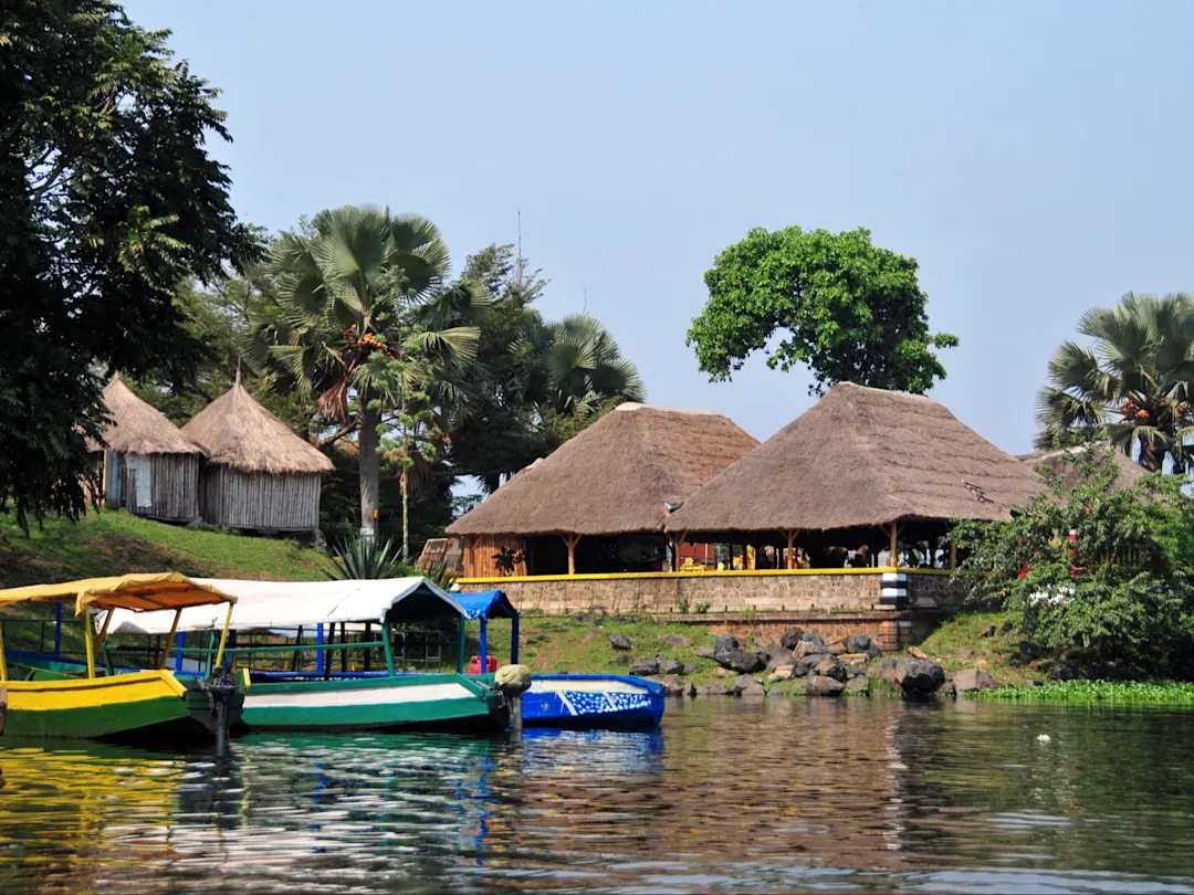 Jinja, Osten, Uganda Bunte Boote vor traditionellen strohgedeckten Hütten am Ufer des Nileriver. Jinja, Osten, Uganda.