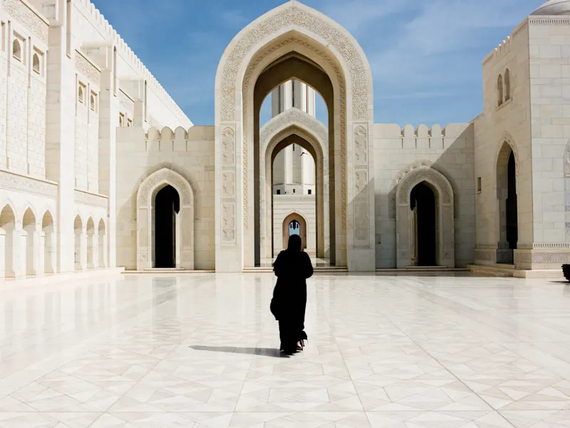 Eine Frau in schwarzer Abaya steht in einem eleganten Innenhof mit beeindruckenden Bögen. Maskat, Maskat, Oman.