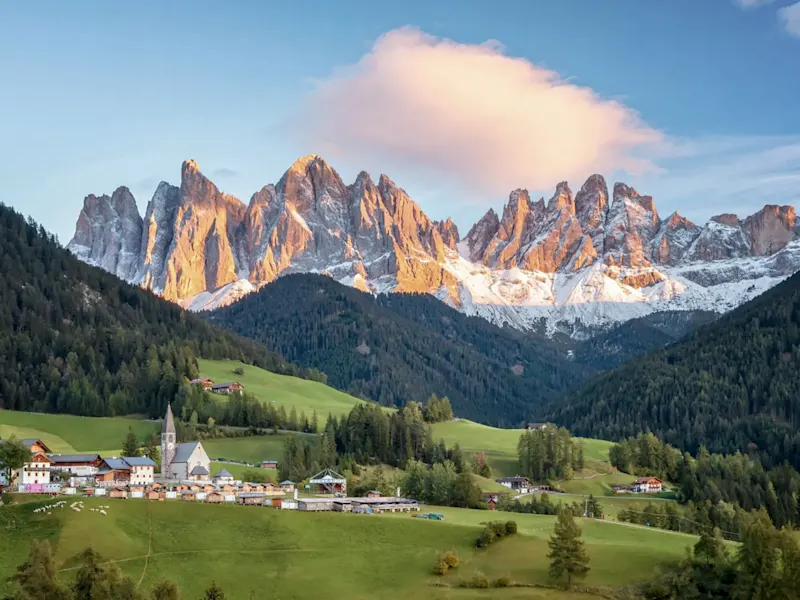 Italien, Dolomiten, Familienreise Dorf im grünen Tal mit schneebedeckten Bergen und Kirche mit hohem Turm. Dolomiten, Italien.