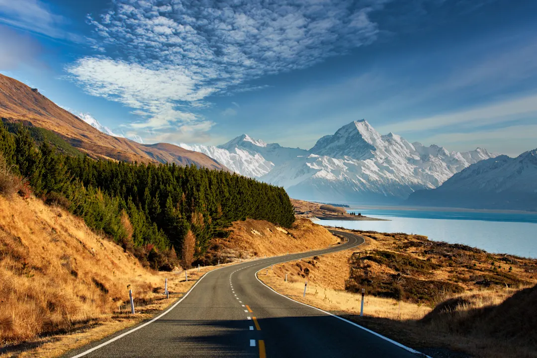 Malerischer Roadtrip des Mt. Cook über eine kurvenreiche Straße und den Lake Pukaki an einem sonnigen Tag in Neuseeland

