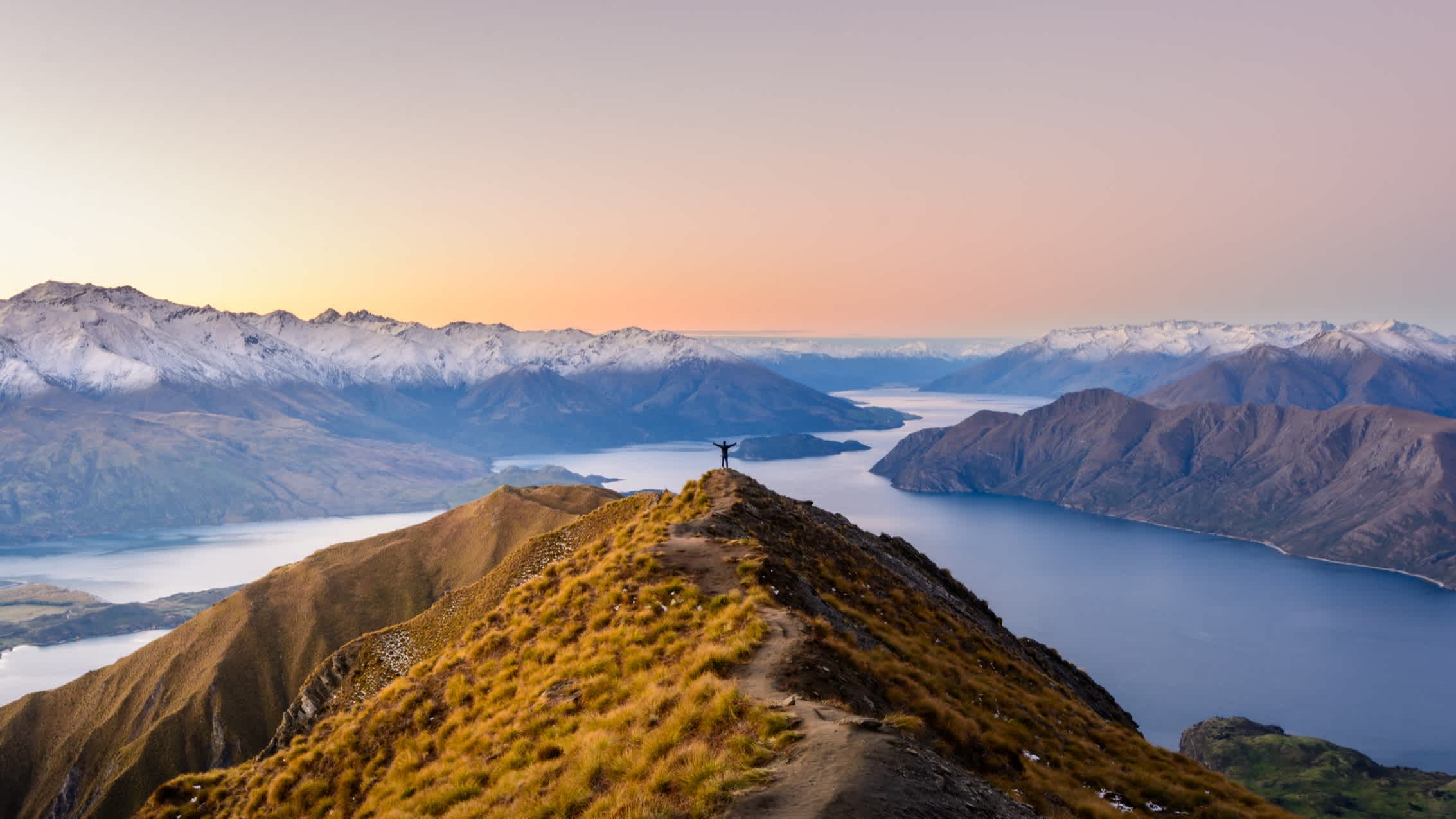 Personne les bras tendus sur le Roy's Peak avec vue sur le paysage, en Nouvelle-Zélande.
