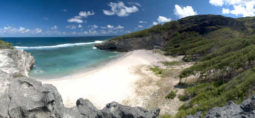 Plage de sable blanc entourée d'un paysage naturel de rochers et d'arbres à Rodrigues, Maurice