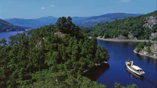 Blick auf einen alten Dampfer auf den See Loch Katrine mit üppiger Vegetation und Hügellandschaft