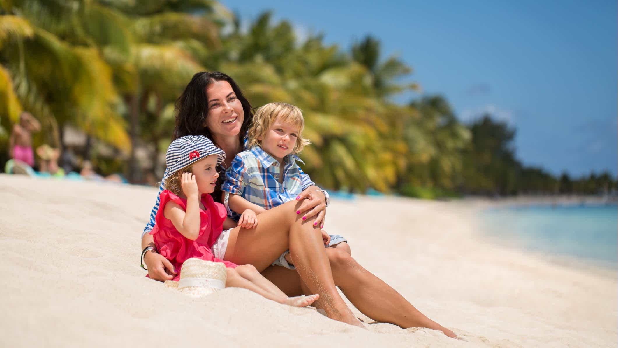 Mère avec ses deux enfants en bas âges assis sur le sable blanc au bord de l'eau sur une plage à l'île Maurice
