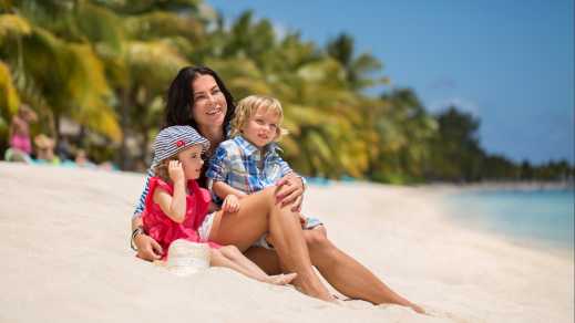 Mère avec ses deux enfants en bas âges assis sur le sable blanc au bord de l'eau sur une plage à l'île Maurice
