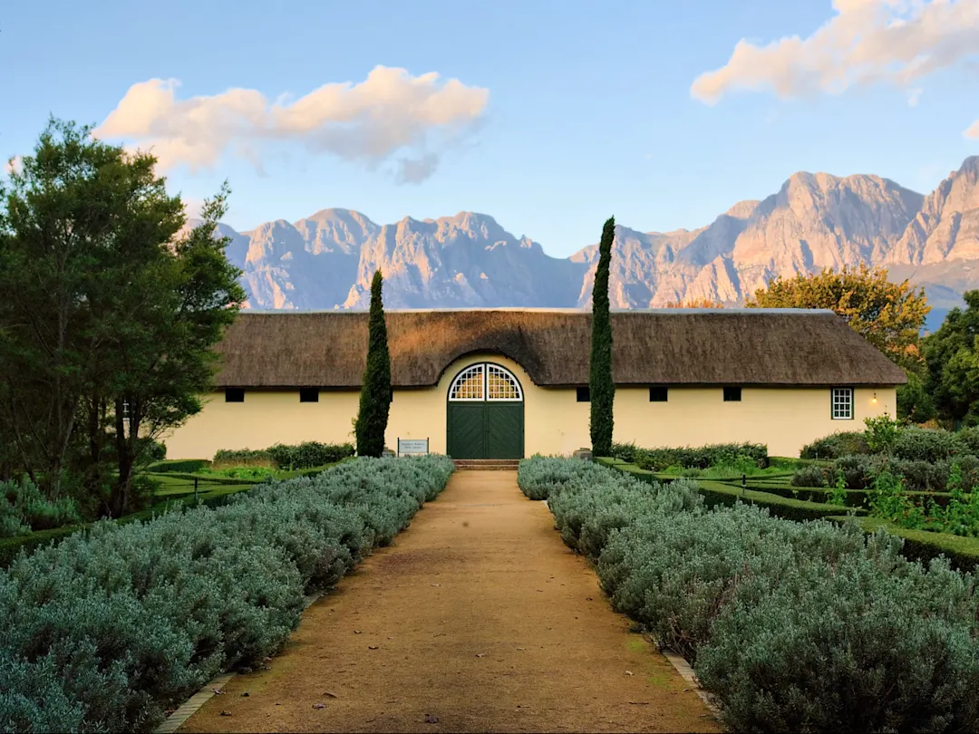 Historisches Gutshaus mit Reetdach vor felsiger Bergkulisse. Stellenbosch, Westkap, Südafrika.