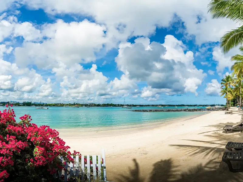 Mauritius, Flitterwochen Strand mit rosa Blumen, Palmen, Liegestühlen und ruhigem türkisfarbenem Wasser. Mauritius.