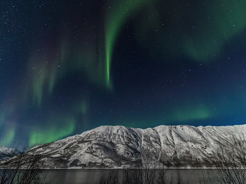 Grüne Polarlichter tanzen über schneebedeckten Bergen und einem dunklen Sternenhimmel. Norwegen.