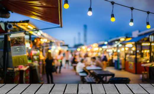 Bild des Holztisch vor dekorativen Outdoor-Zeichenfolge Lichter Lampe im Nachtmarkt mit Unschärfe Menschen, Festival und Urlaub Konzepte, kann für die Anzeige oder die montage Ihrer Produkte. 