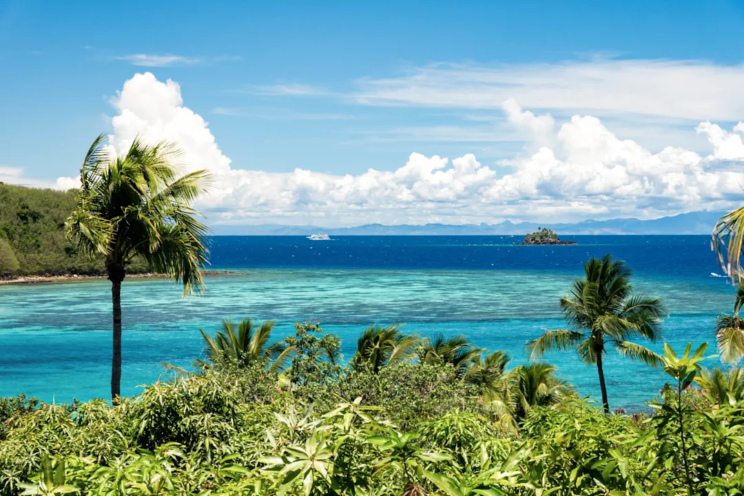 Eine tropische Insel mit üppigem Grün und Kokospalmen ragt unter einem klaren, strahlenden Himmel über den Ozean hinaus
