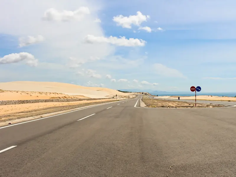 Vietnam, Roadtrip Gepflasterte Straße, Sanddünen, Verkehrsschilder, klarer Himmel mit einigen Wolken. Vietnam.