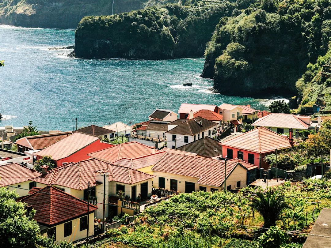 Rote Dächer der Häuser in einer grünen Landschaft mit einem Wasserfall und dem Meer, Seixal, Madeira, Portugal.

