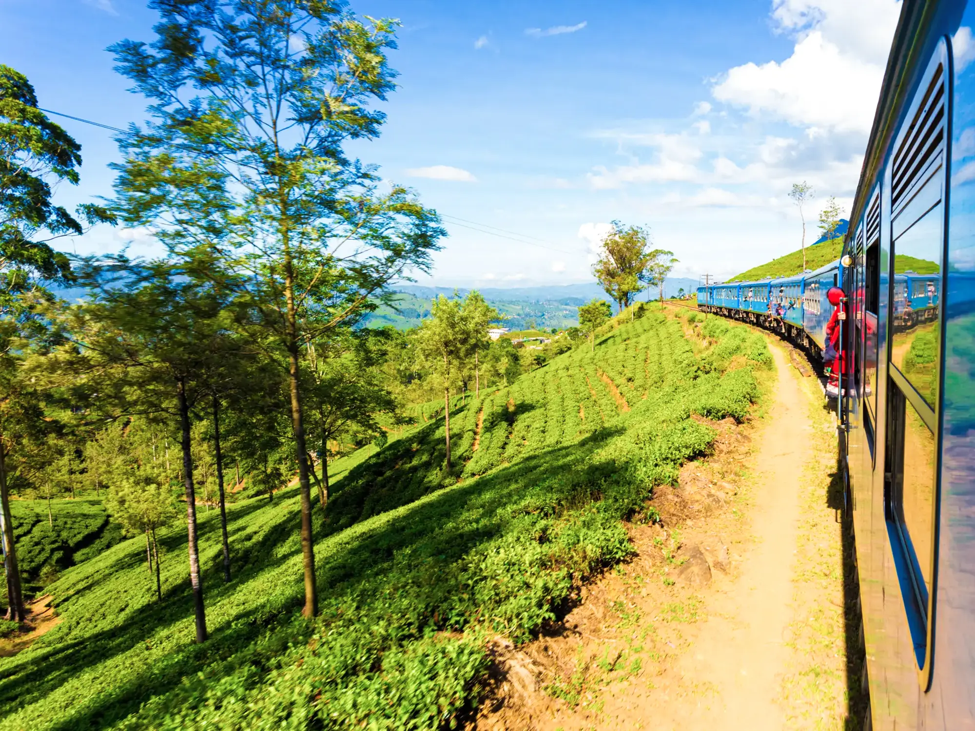 Blauer Zug durch grüne Teeplantagen und hügelige Landschaft. Zentralprovinz, Sri Lanka.